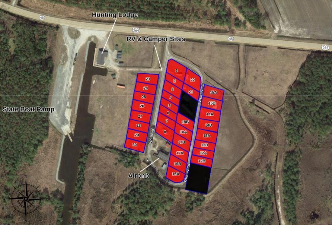 Aerial view of a site plan with red outlined lots around a central dark building on a dirt landscape.