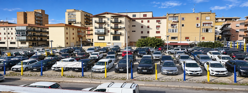 Parcheggio pieno di auto davanti ai palazzi in una giornata di sole.