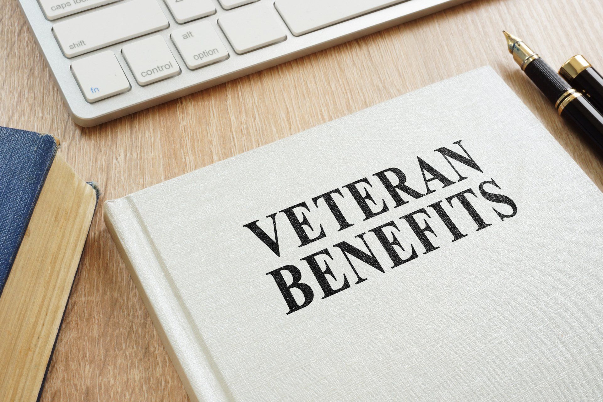A book titled veteran benefits is sitting on a wooden table next to a pen.