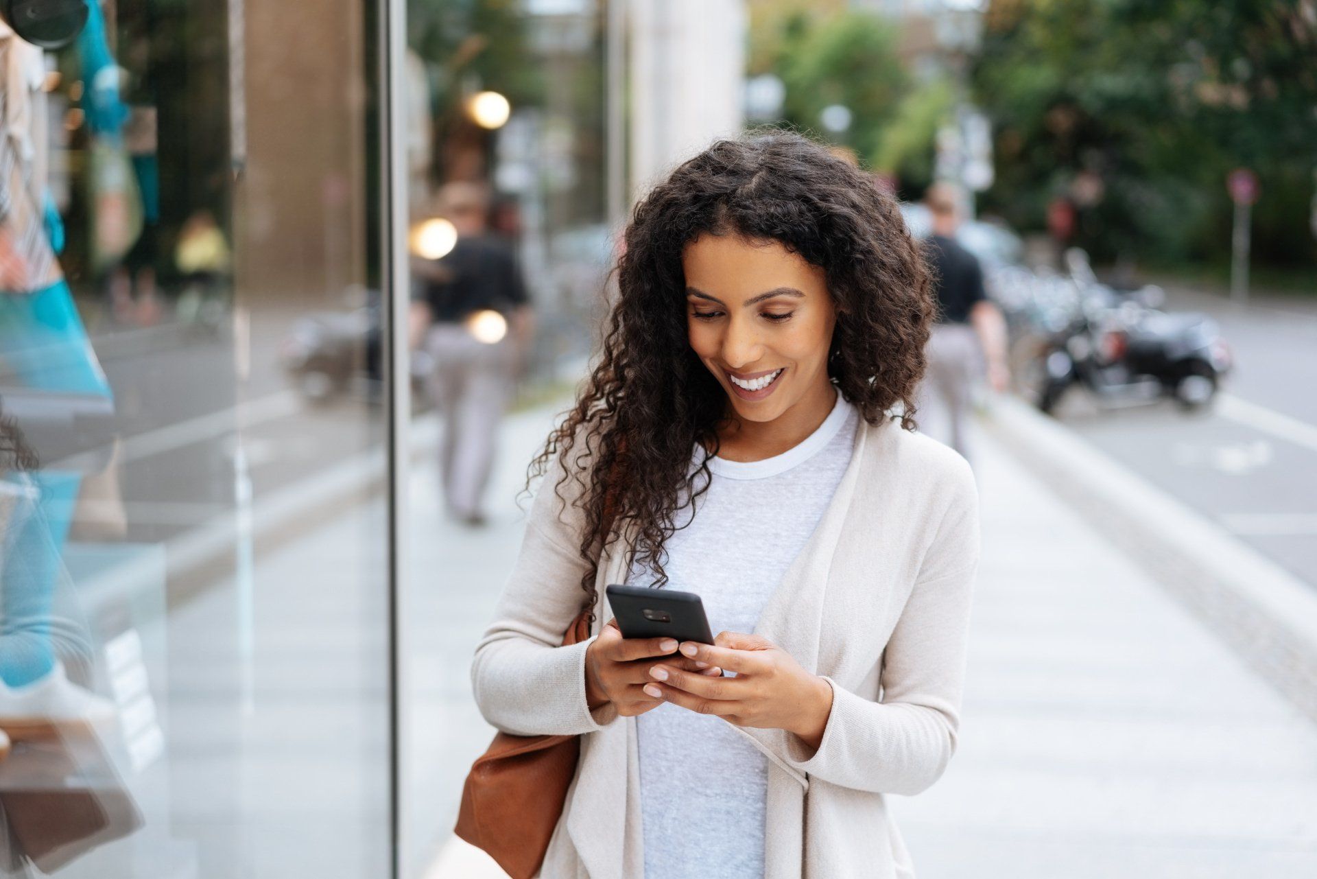 A woman is standing on a sidewalk looking at her cell phone.