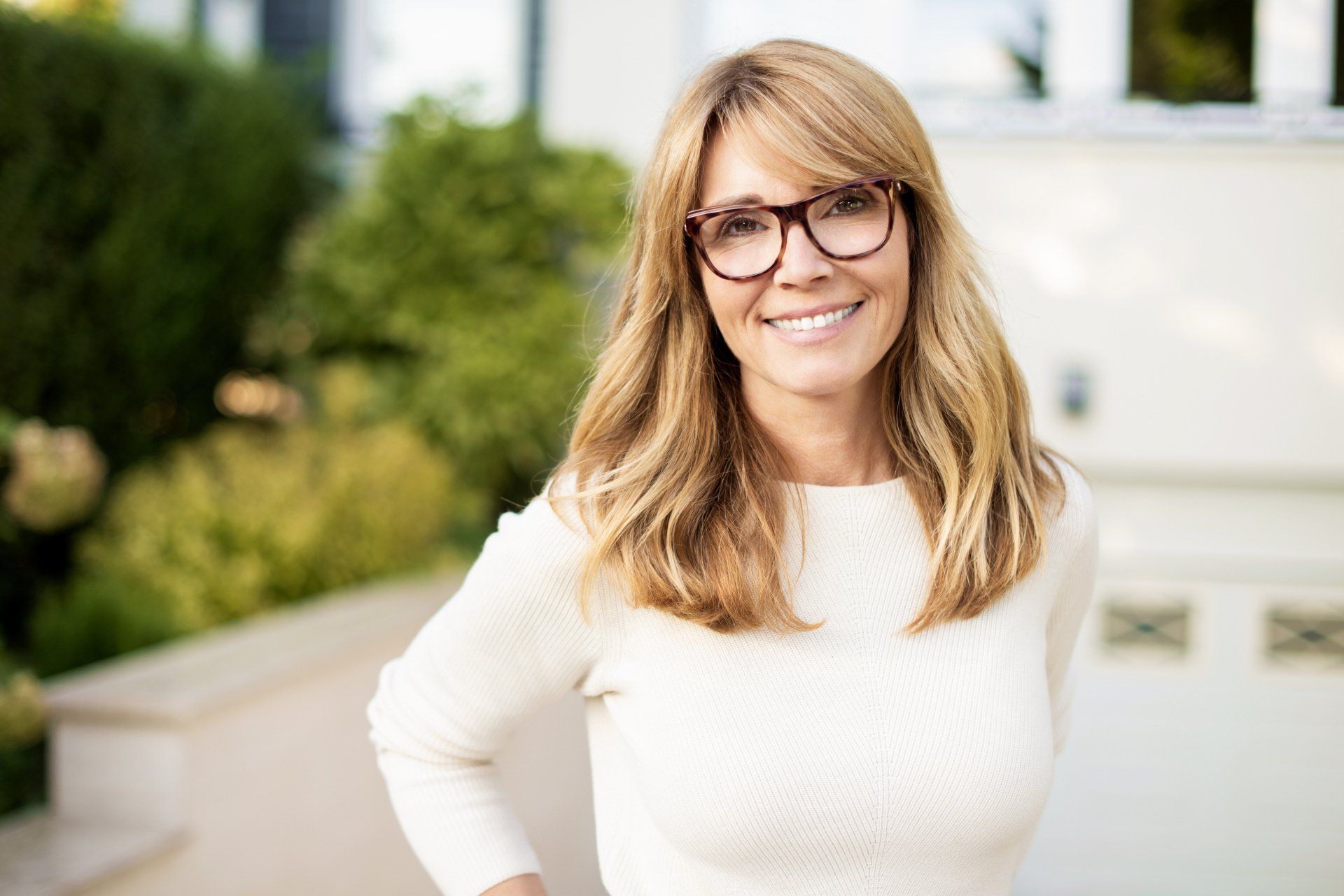 A woman wearing glasses and a white sweater is smiling for the camera.