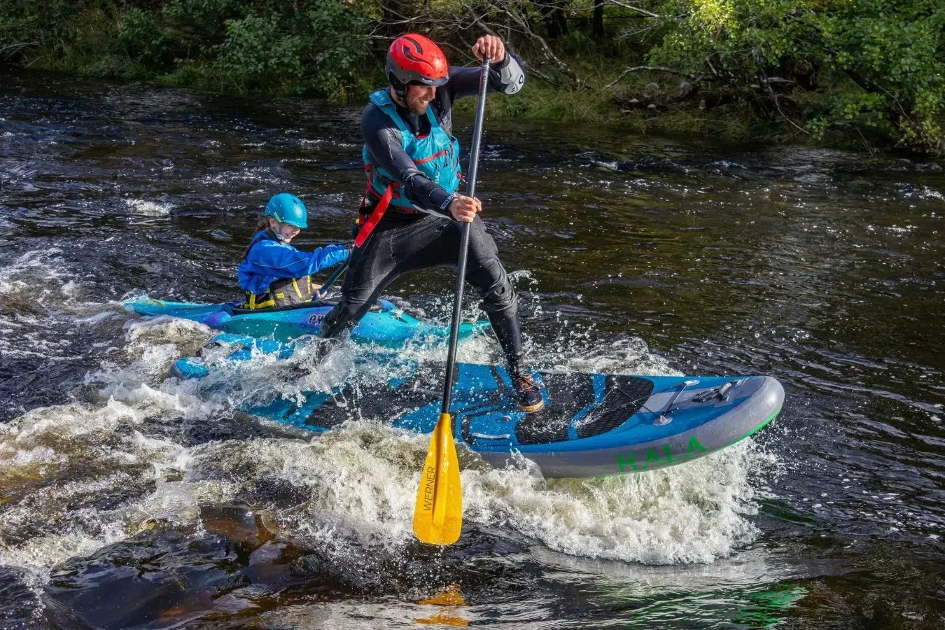 A man is paddling a kayak down a river.