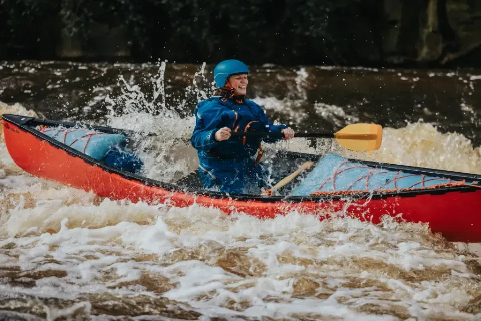Mae dyn yn padlo canŵ coch trwy afon.