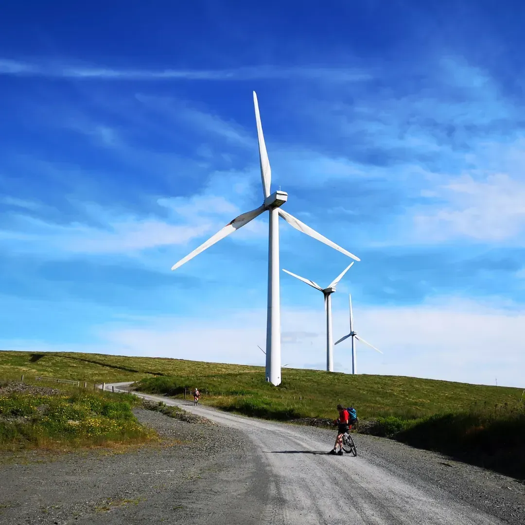 A person riding a bike down a dirt road with windmills in the background