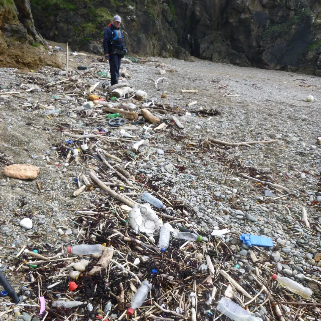 A man is standing on a beach covered in trash.