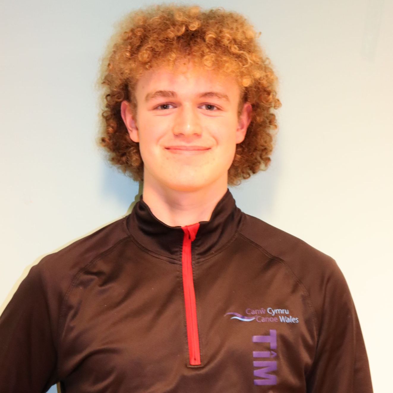 A young man with curly hair is wearing a shirt that says tim