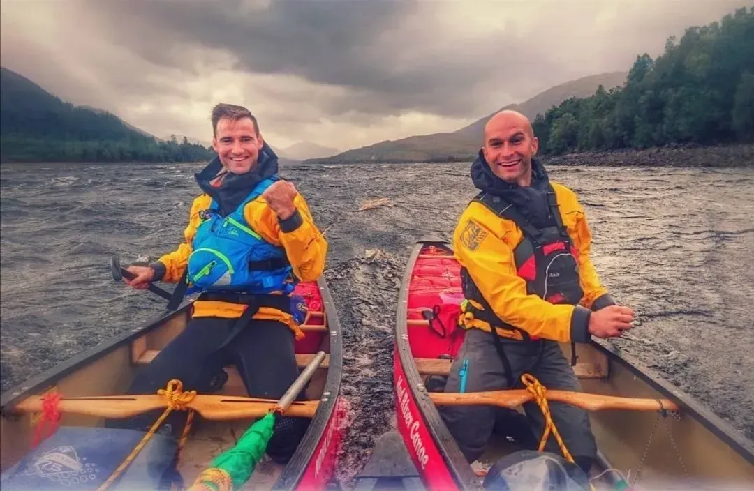 Two men are sitting in a canoe on a river.