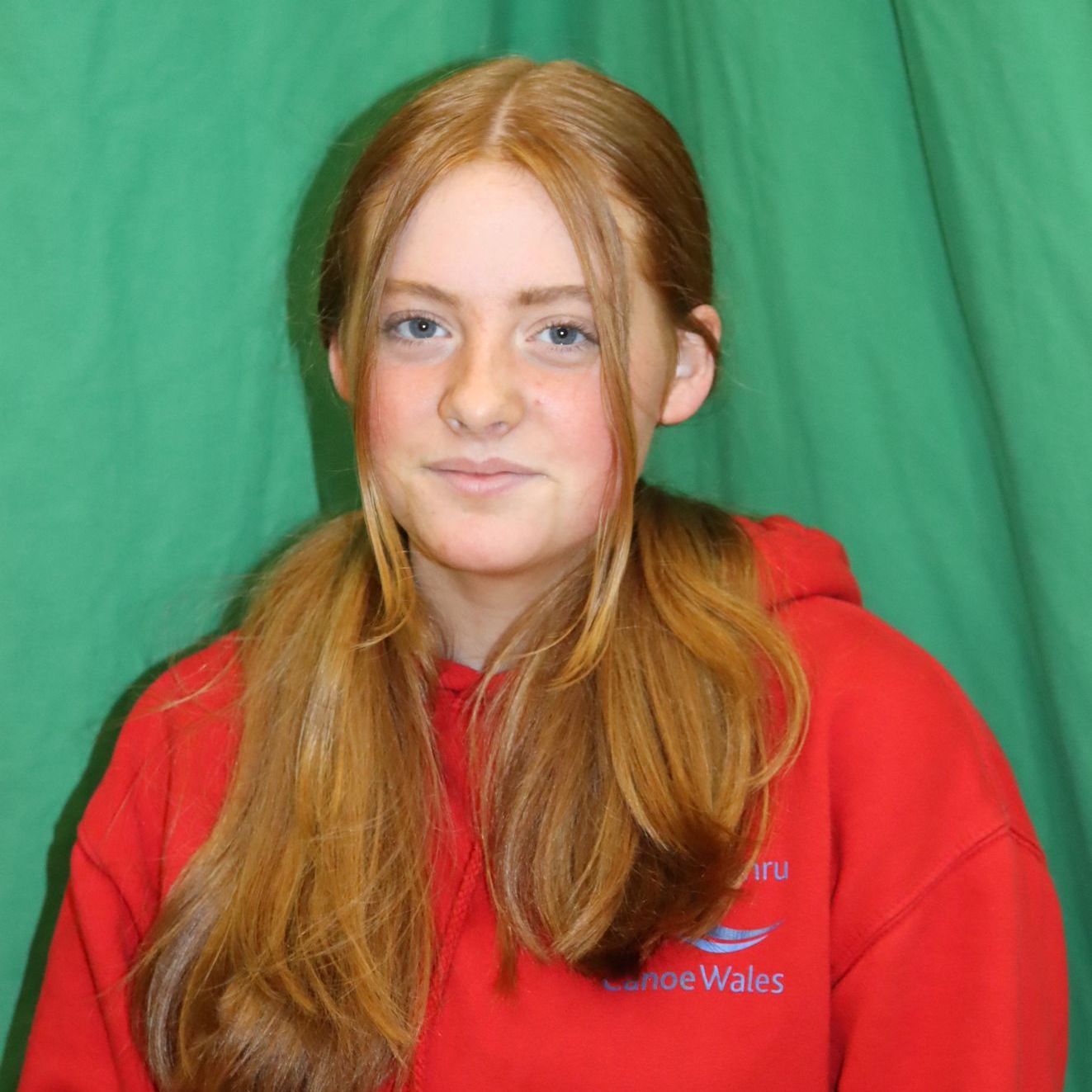 A young girl with long red hair is wearing a red hoodie.