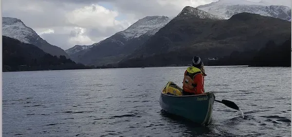 A person is in a canoe on a lake with mountains in the background.