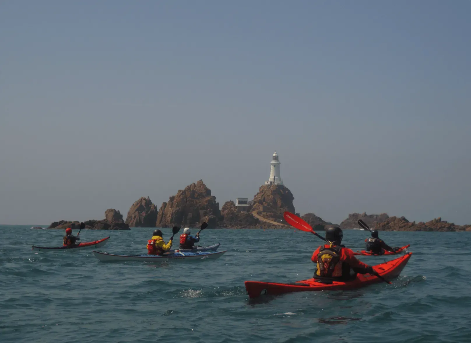 A group of people are kayaking in the ocean near a lighthouse.