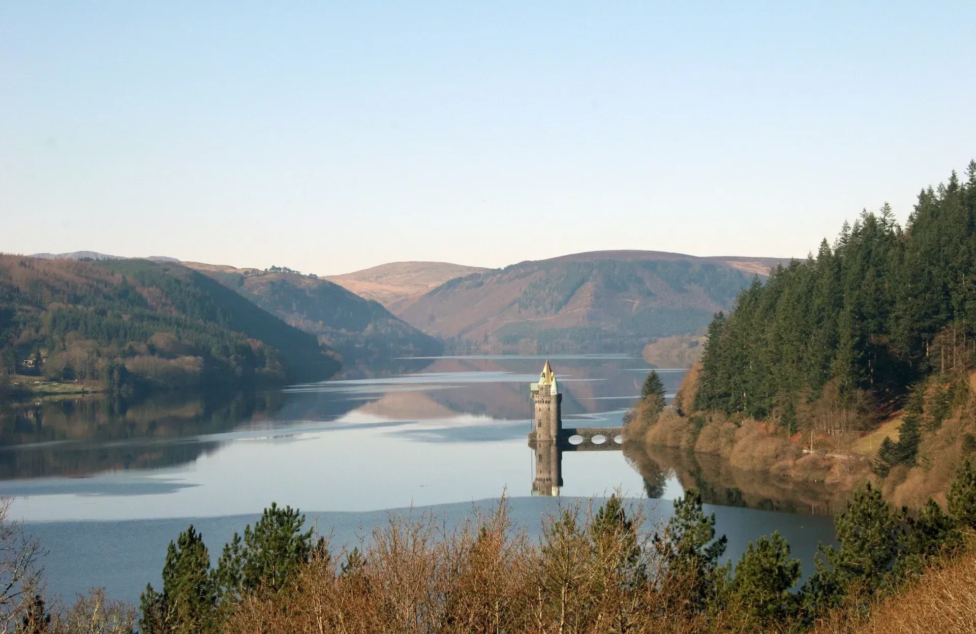 Corff mawr o ddŵr wedi'i amgylchynu gan goed a mynyddoedd