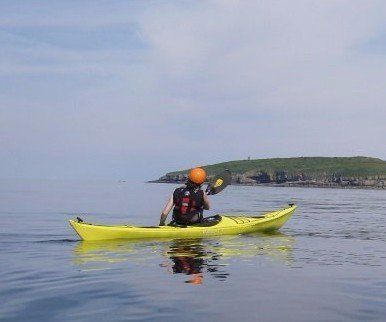 A person is paddling a yellow kayak in the ocean.