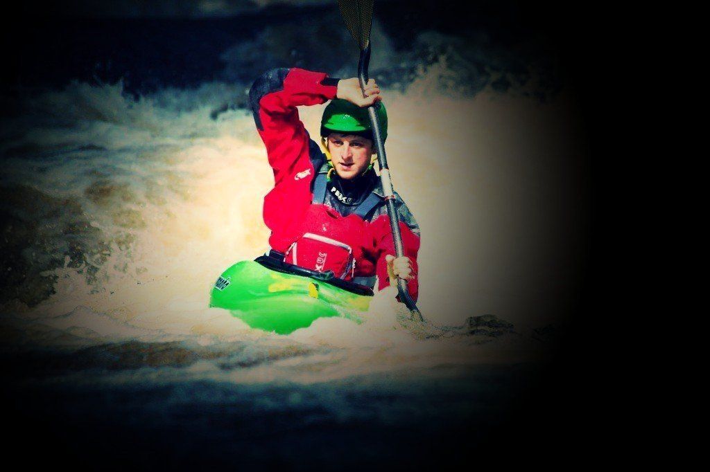 A man in a red jacket is paddling a green kayak