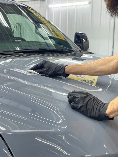 A person is polishing the hood of a blue car.