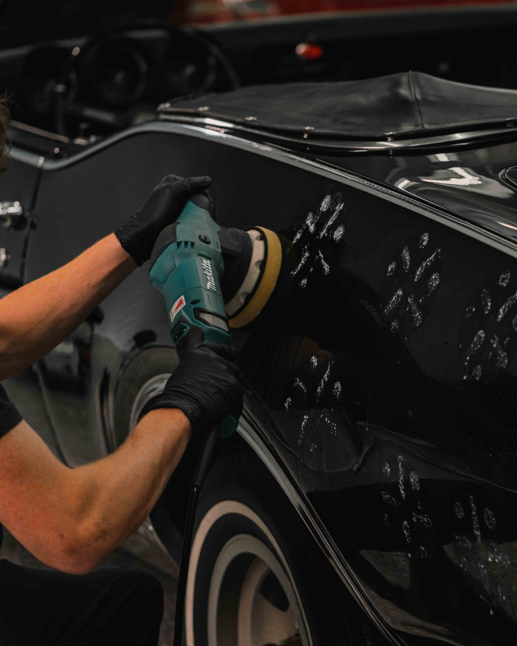 A person wearing black gloves is polishing a black car