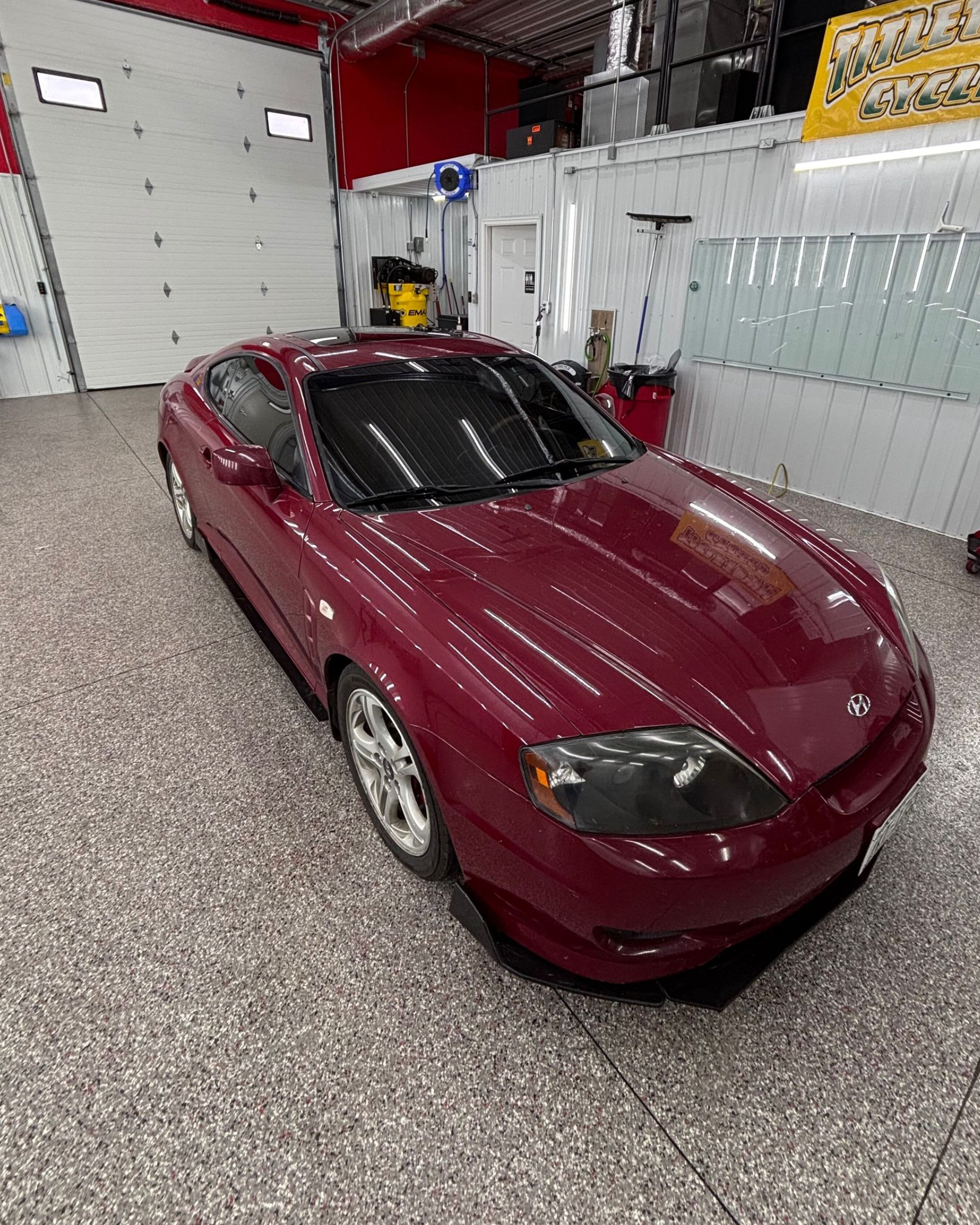 White pickup truck on a red hydraulic lift in a garage with a speckled floor and white walls.