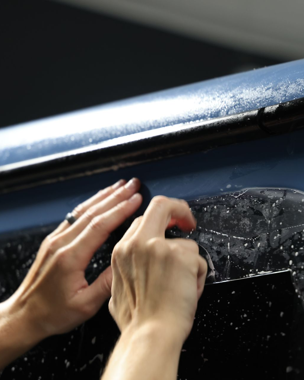 A person wearing black gloves is polishing a black car