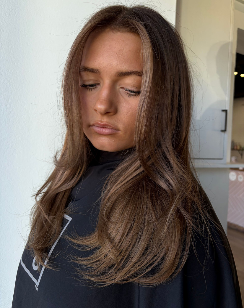 Woman with wavy, brunette hair, ombre style. Light brown at the ends. Inside a salon.