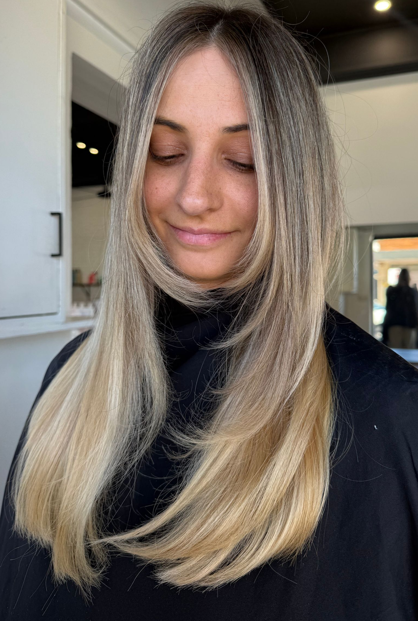 Woman with long, reddish-blonde hair in a salon, wearing a black cape.