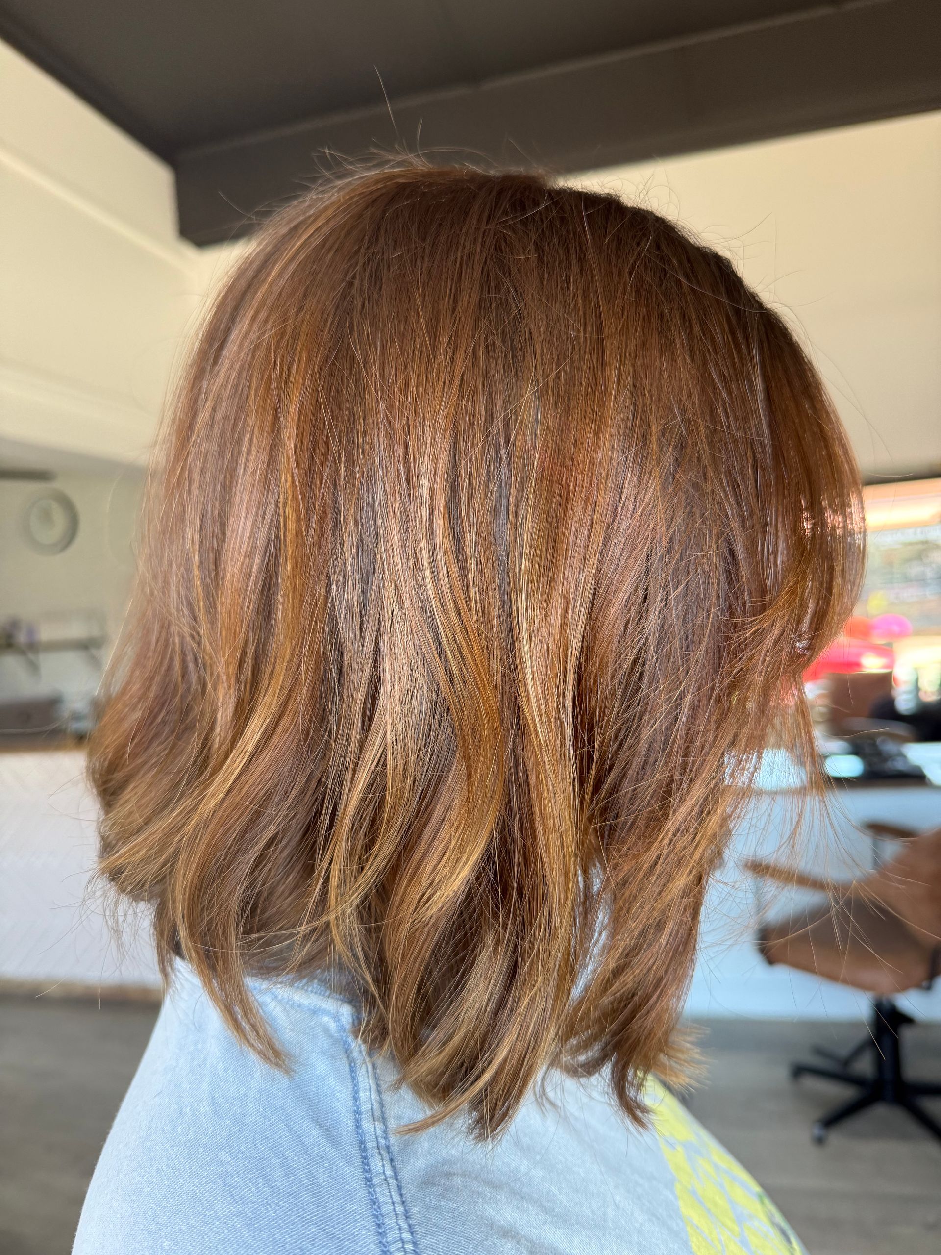Red-orange, straight hair held by a hand with red nail polish, in a salon setting.