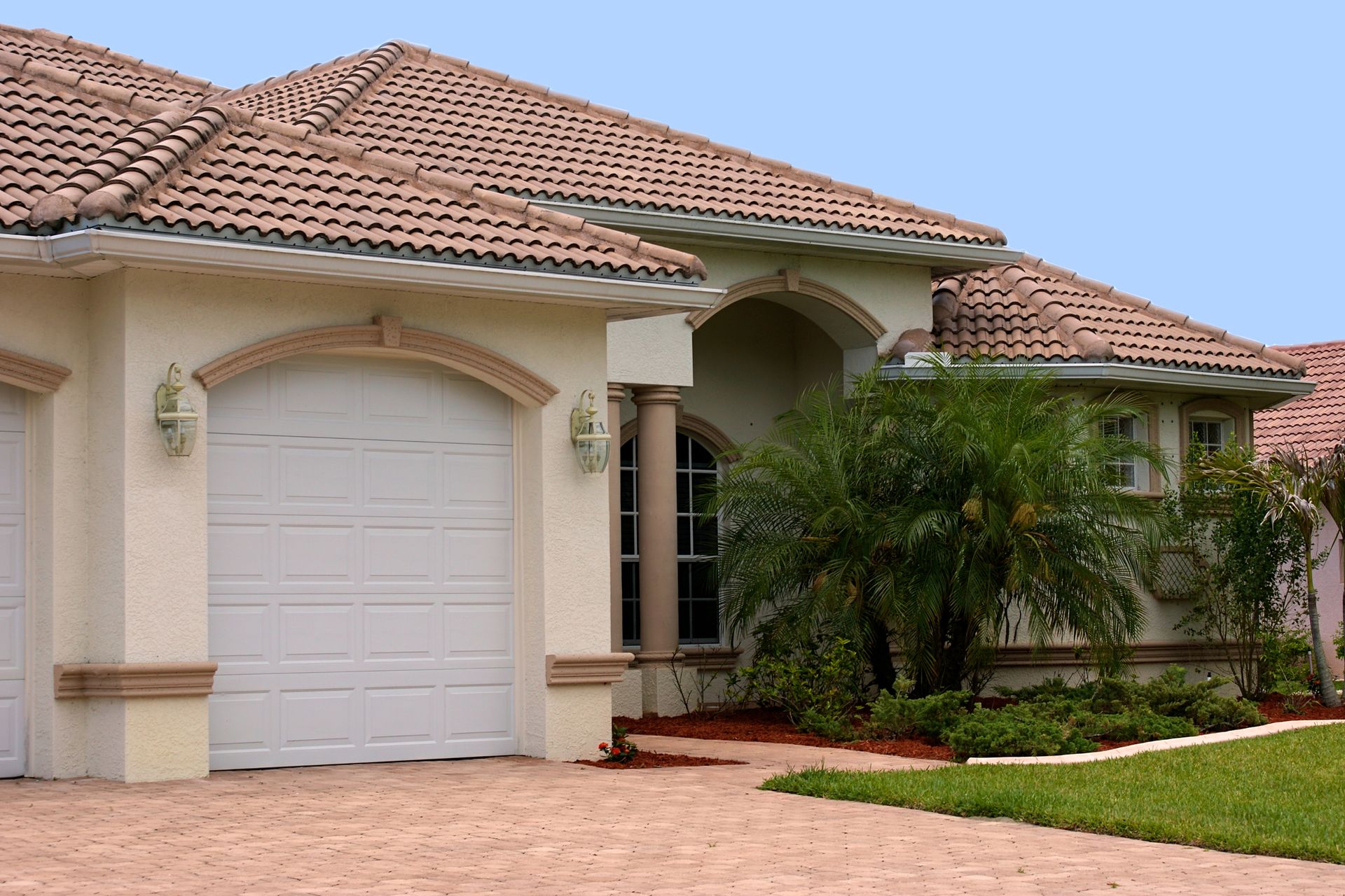 Tan stucco house with a tile roof, white garage door, and a palm tree in front.