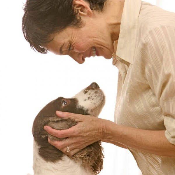 Woman smiles, petting a brown and white dog. White background.