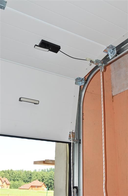 Garage door, partially open, revealing its interior mechanisms, including tracks and a motor, and some wood paneling.