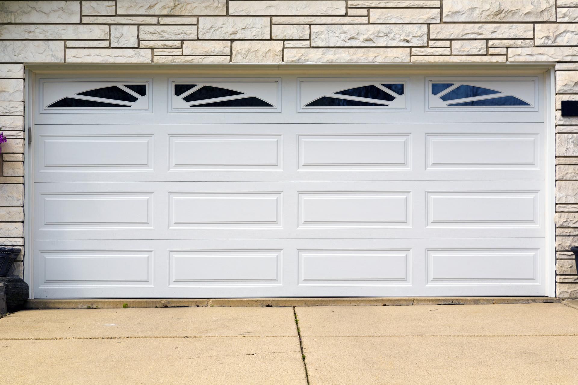White garage door with decorative glass panels, in front of a brick wall and concrete driveway.