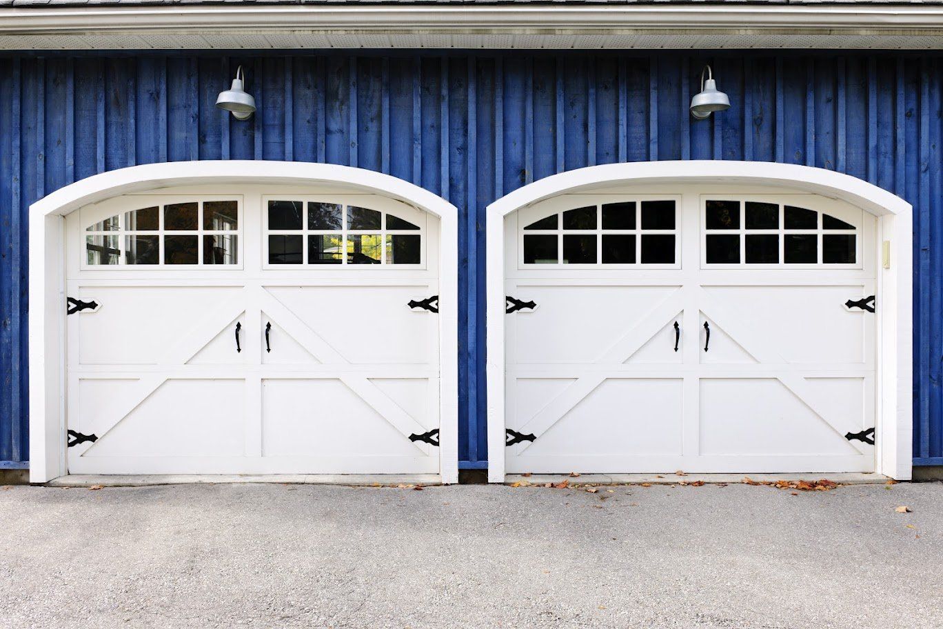 White arched garage doors with black hardware against a blue wooden building.