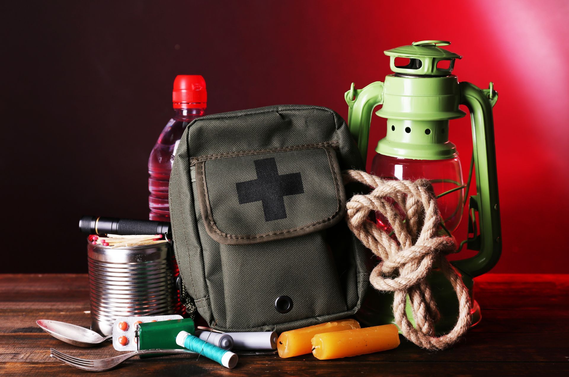 Emergency preparedness kit with first aid, lamp, rope, water, and canned food.