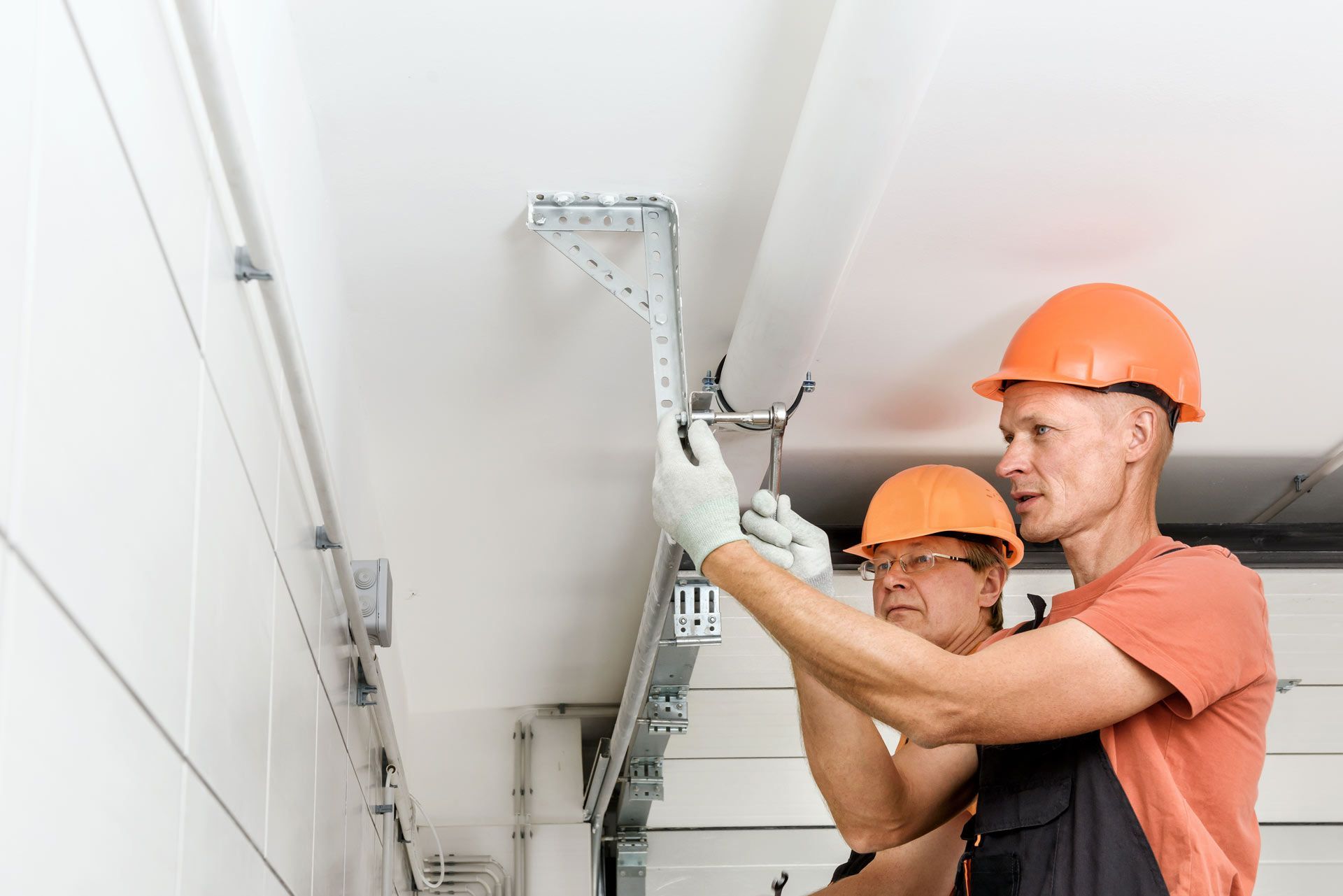 Experienced technicians using professional tools for a garage door repair on a residential ceiling.