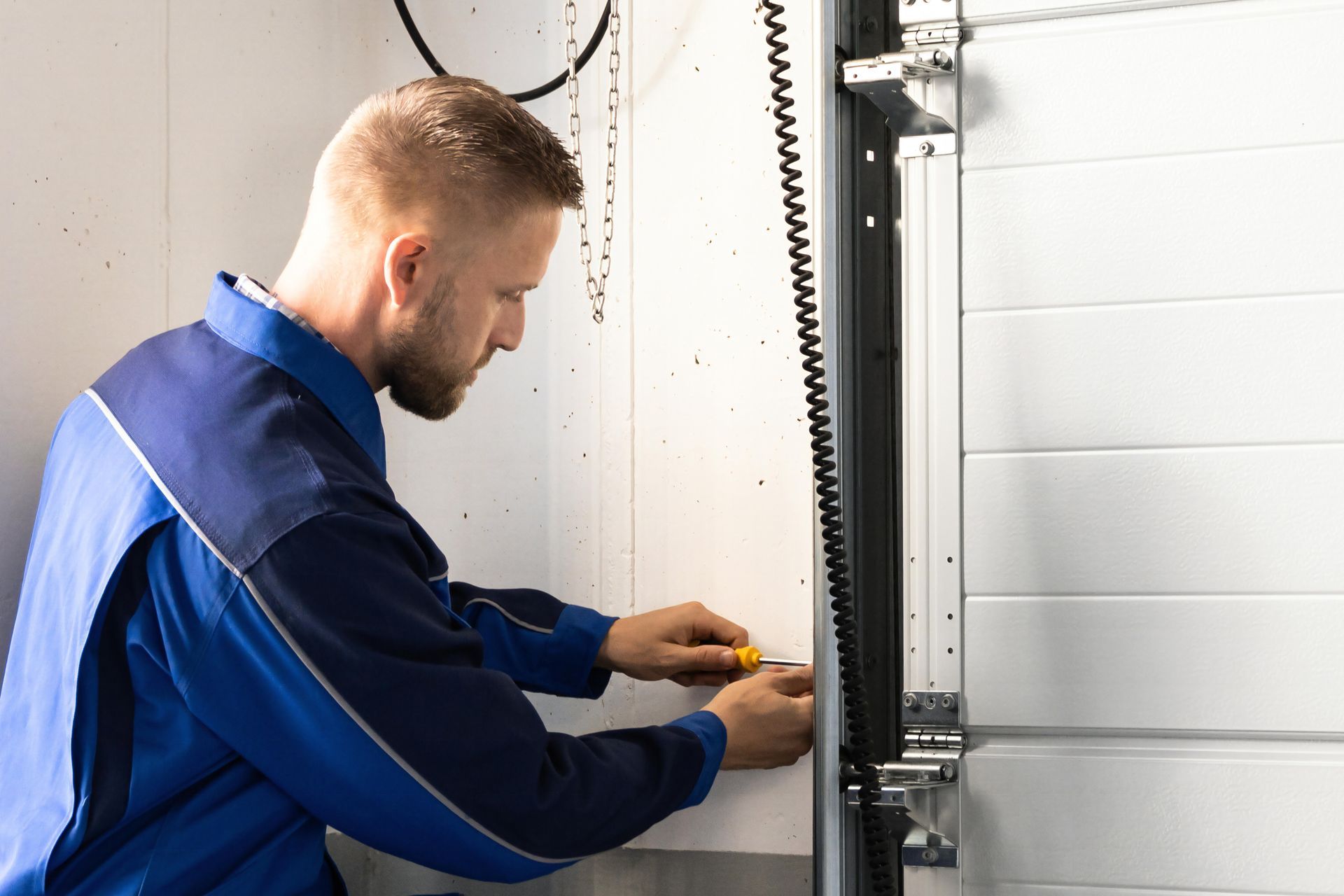 A professional garage door installer is tightening track hardware with a screwdriver tool.