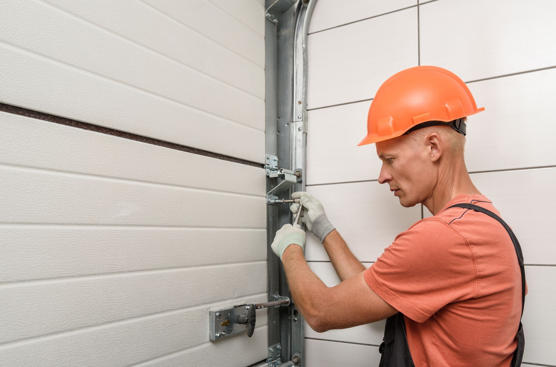A man in an orange hard hat performs garage door system repair in Orange County, CA.