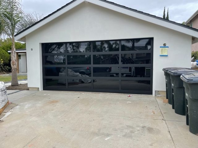 Black glass garage door on white house with trash bins.