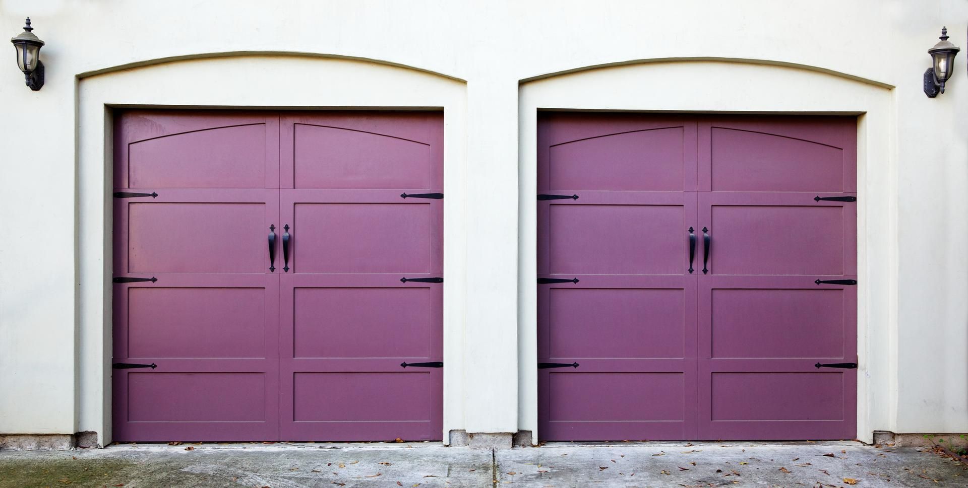 Two purple garage doors with black hardware in a white stucco facade.