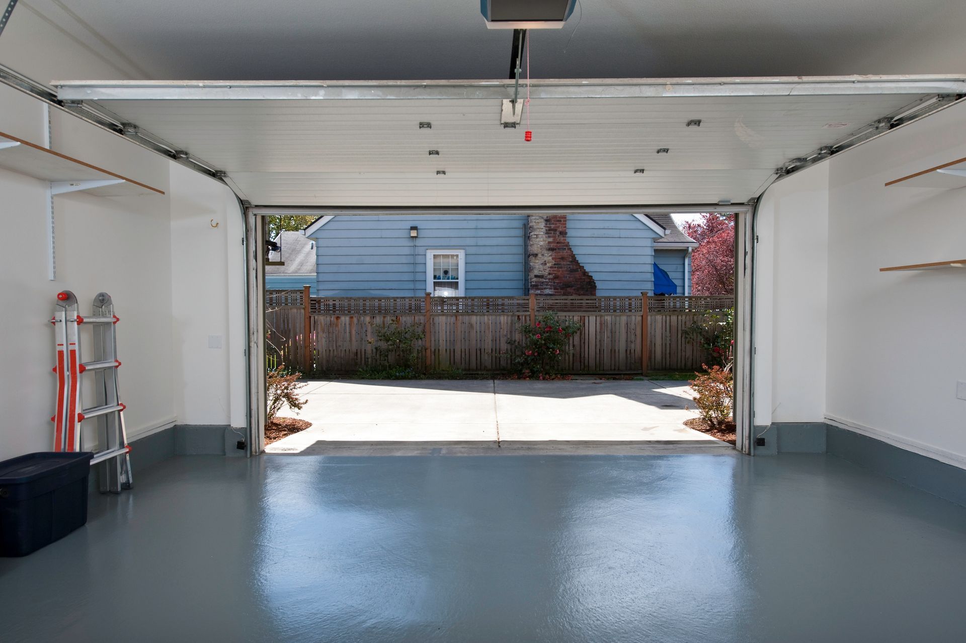 Empty garage with open door, gray floor, white walls, leading to backyard.
