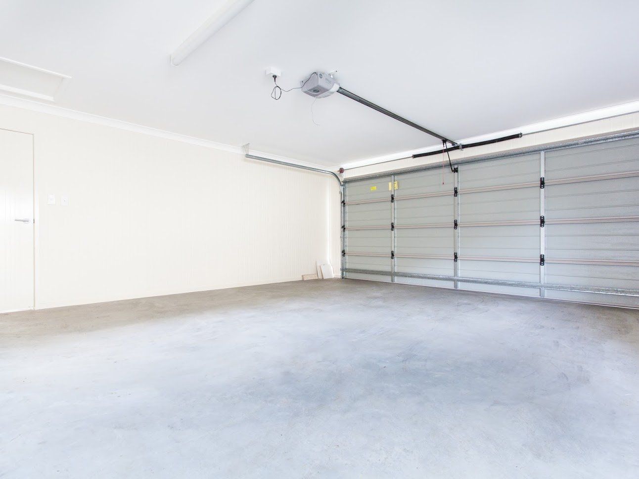 Empty, spacious garage with gray concrete floor, white walls, and closed silver garage door.