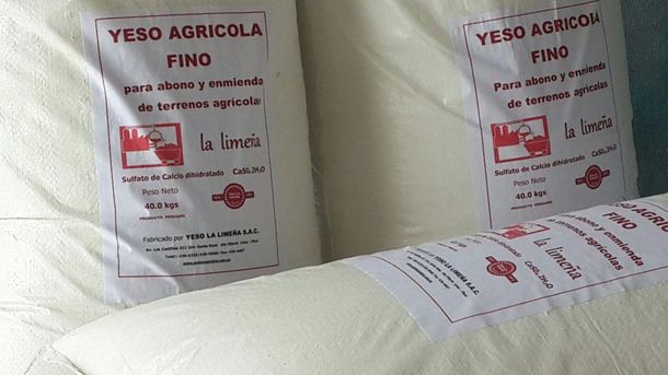 Sacos apilados de yeso blanco con la etiqueta “YESO AGRÍCOLA Fino” en un estante de un almacén.
