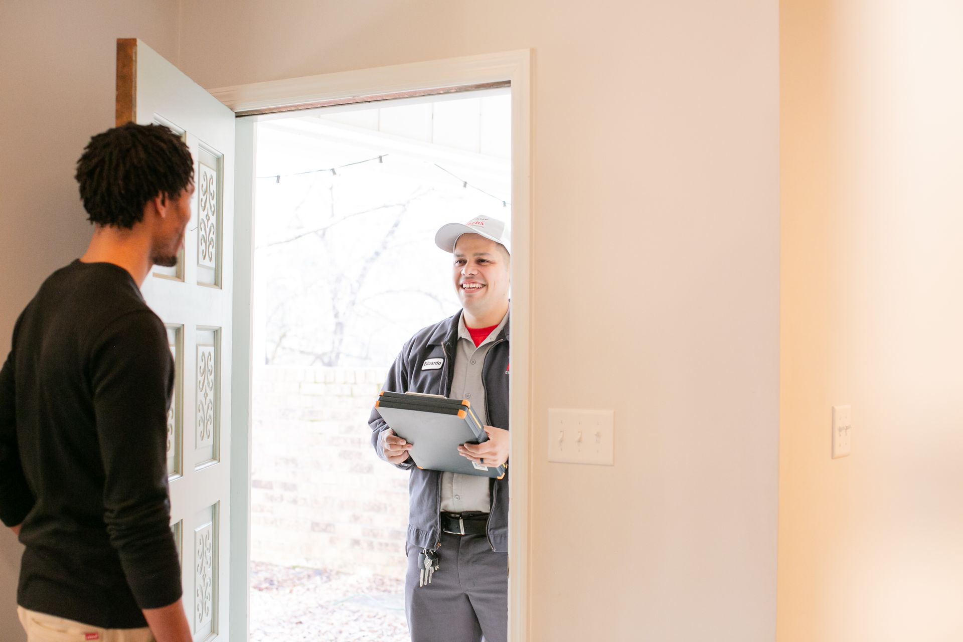 Delivery worker at an open front door, holding a package and talking with a resident inside.