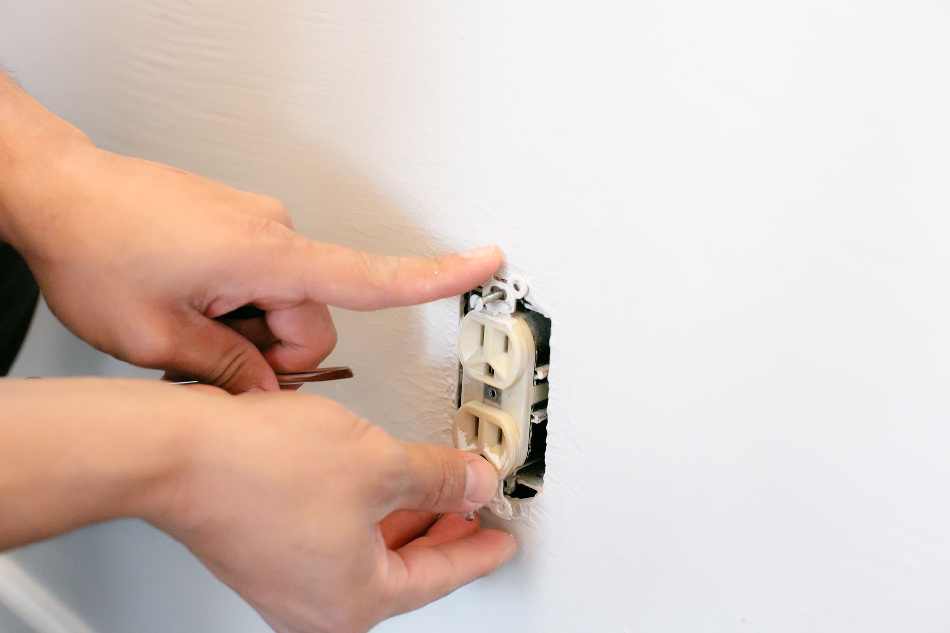 Hands installing a wall electrical outlet with a screwdriver.