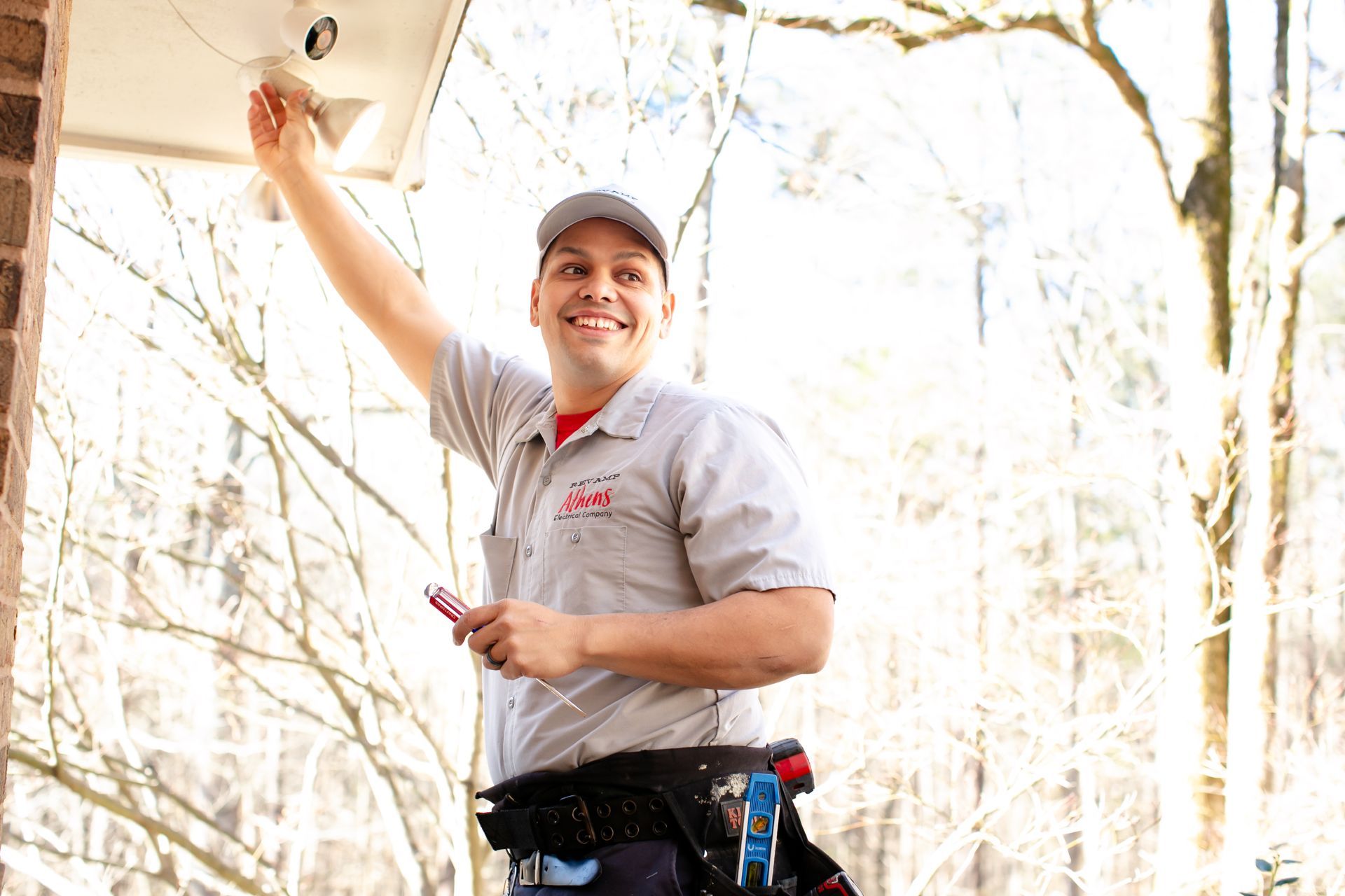 Worker in a hard hat smiling while holding tools in a bright wooded area