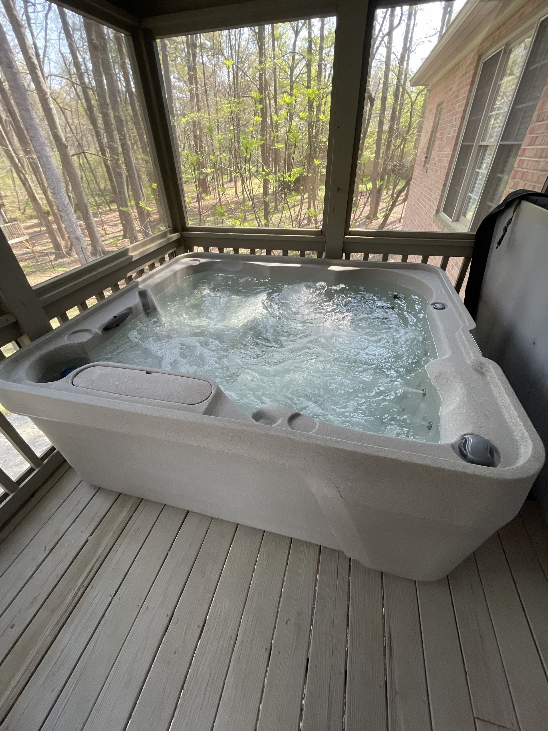 Foaming hot tub on a screened porch overlooking trees