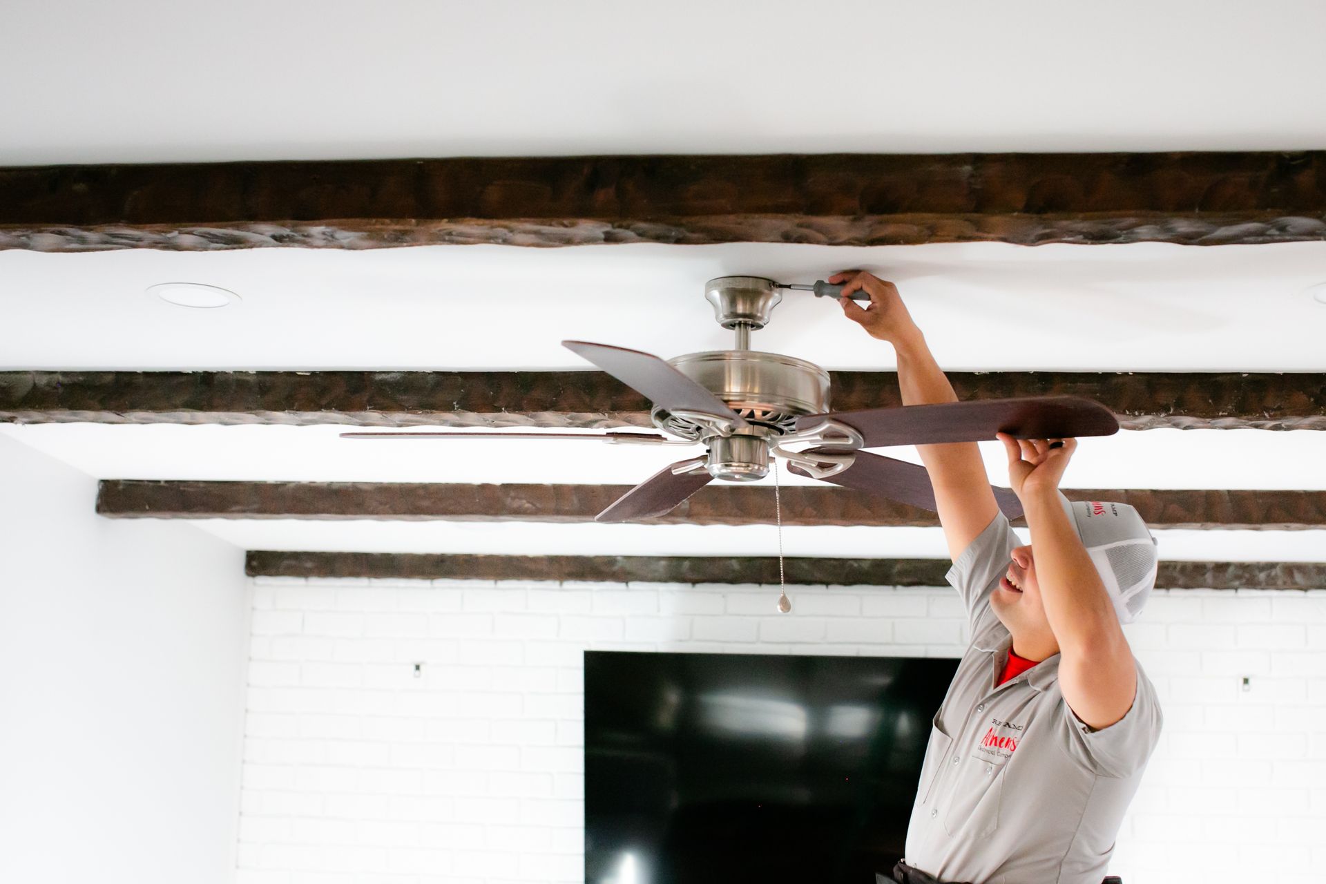 Person adjusting a ceiling fan on white ceiling beams in a bright room