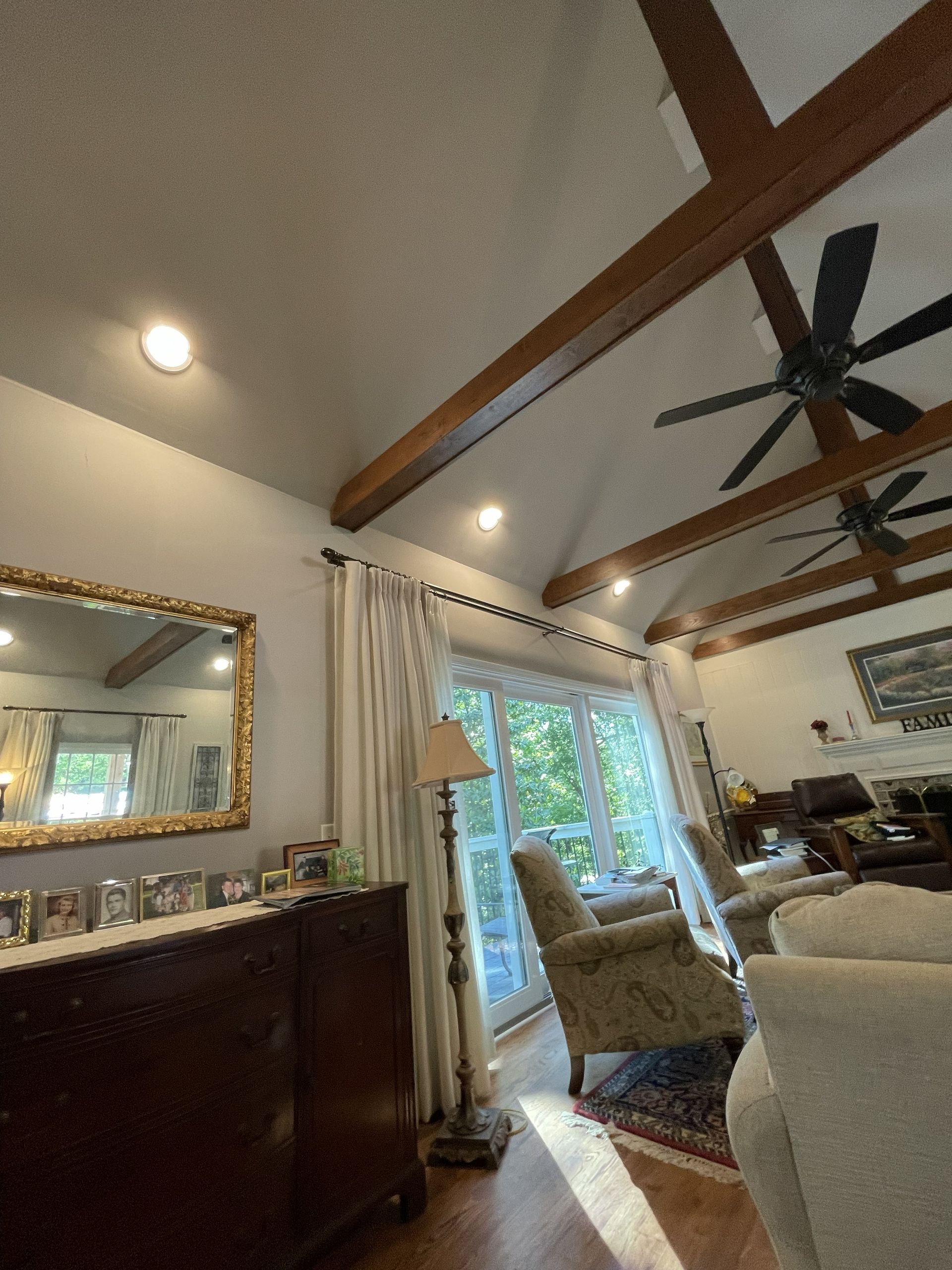 Bright living room with vaulted ceiling, ceiling fans, large mirror, and French doors with curtains.