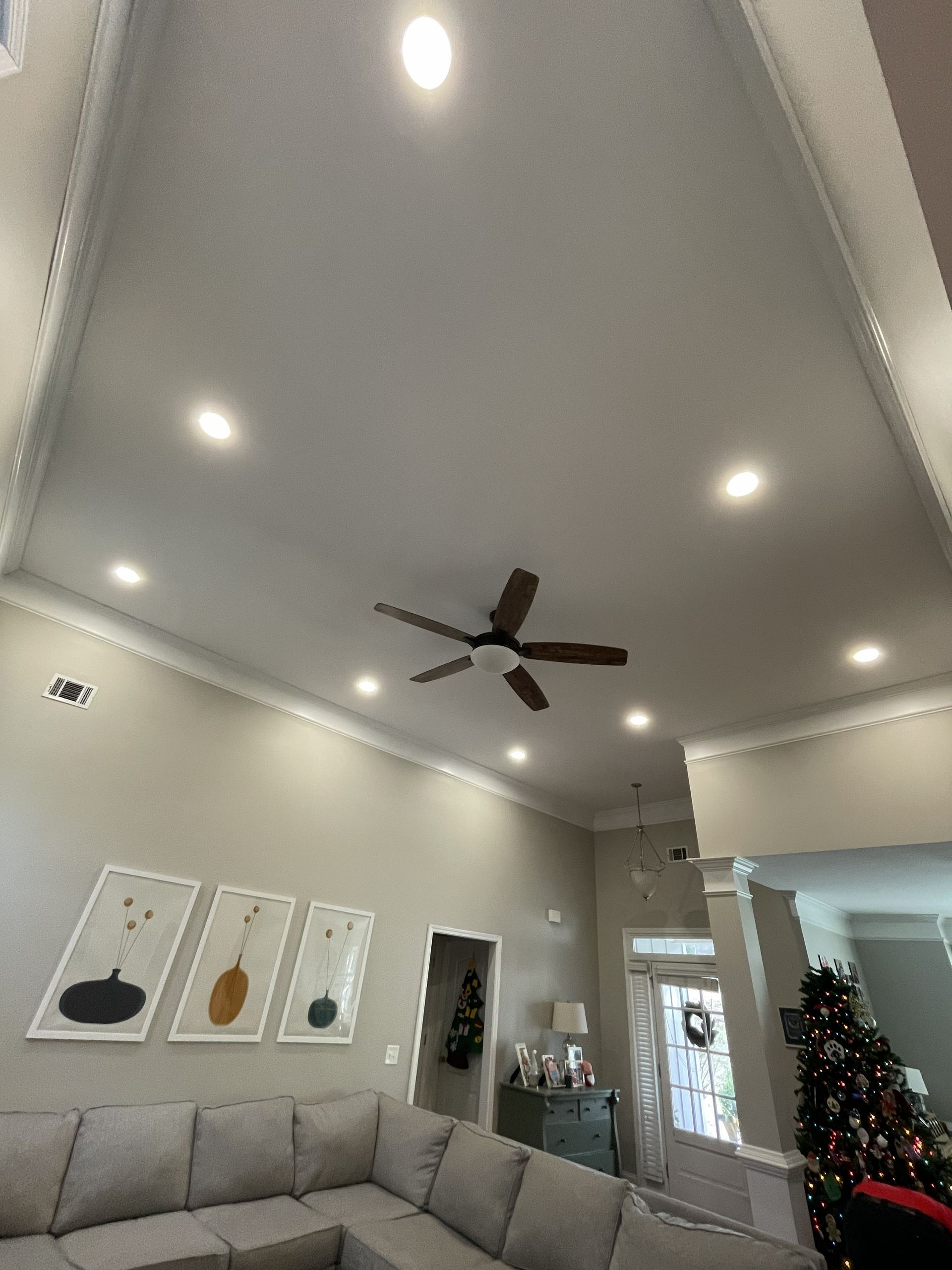 Living room with vaulted ceiling, recessed lights, ceiling fan, gray sectional, wall art, and Christmas tree.