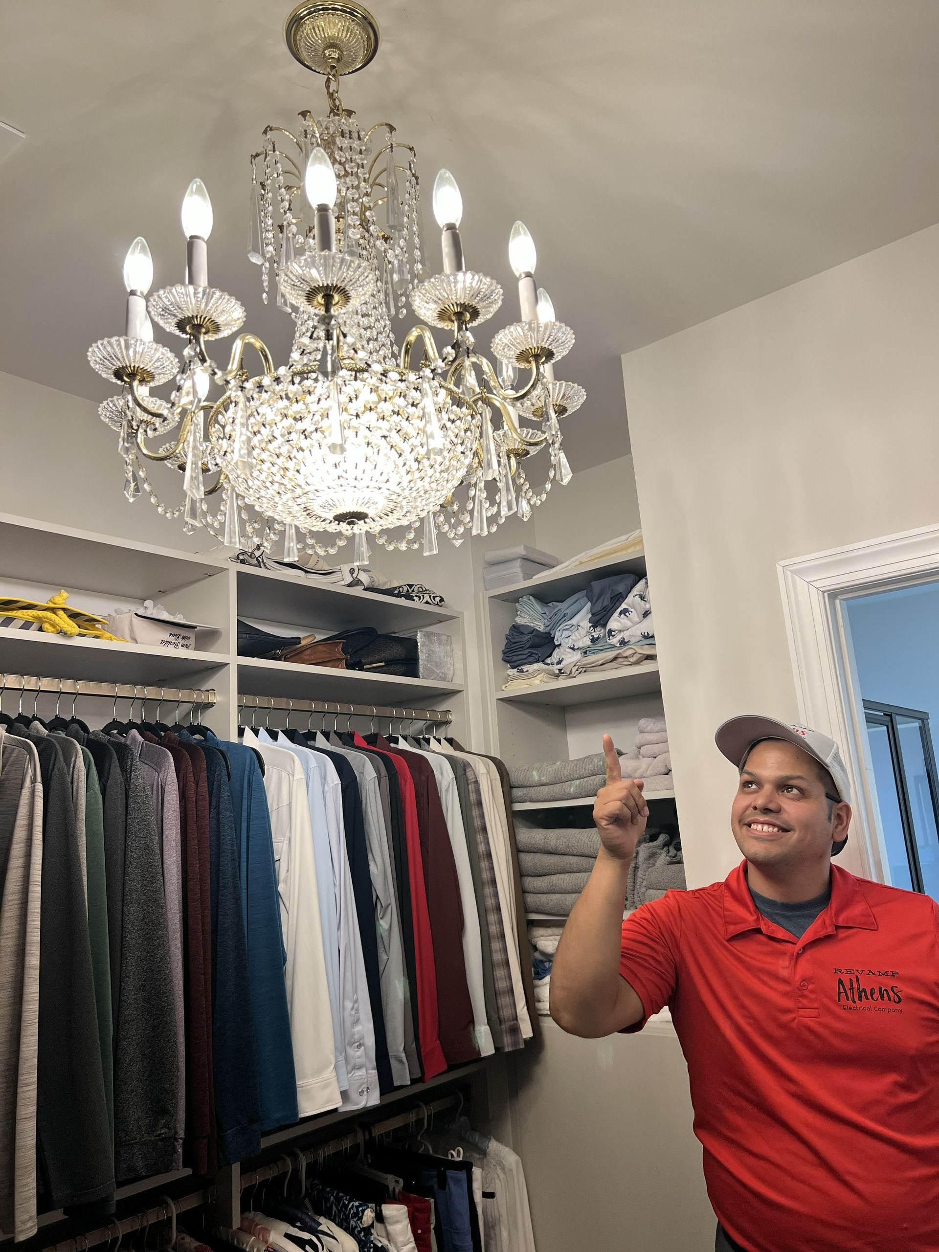 Man in a red polo pointing up beside a crystal chandelier in a walk-in closet