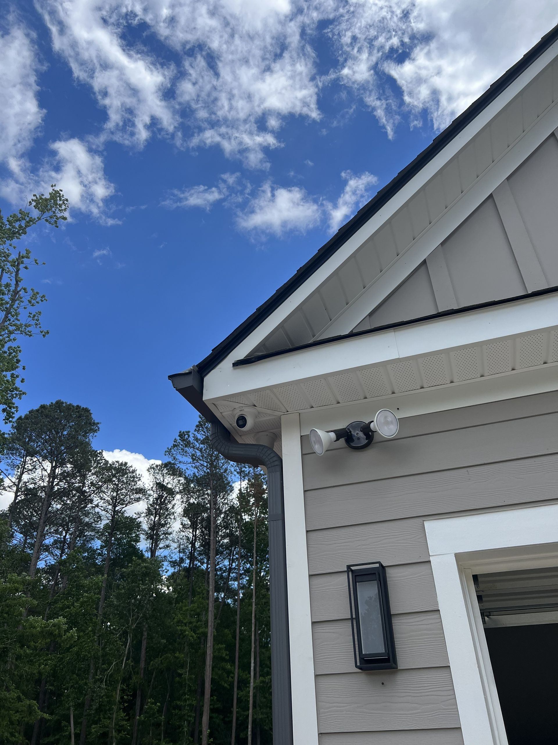 House exterior with white siding, gray trim, security camera, and blue sky with clouds