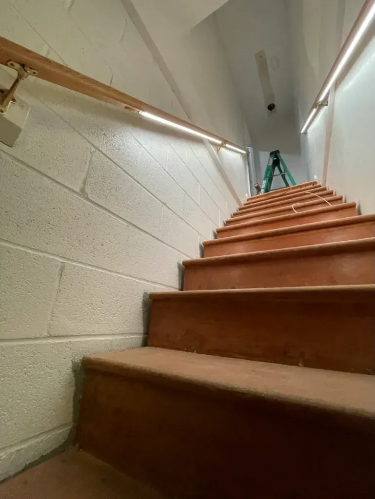 Looking up a narrow indoor staircase with brown wooden steps and beige cinderblock walls