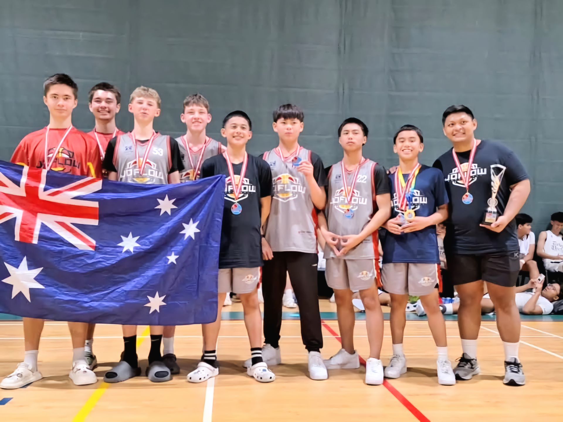 A group of young men are standing on a basketball court holding a flag and medals.