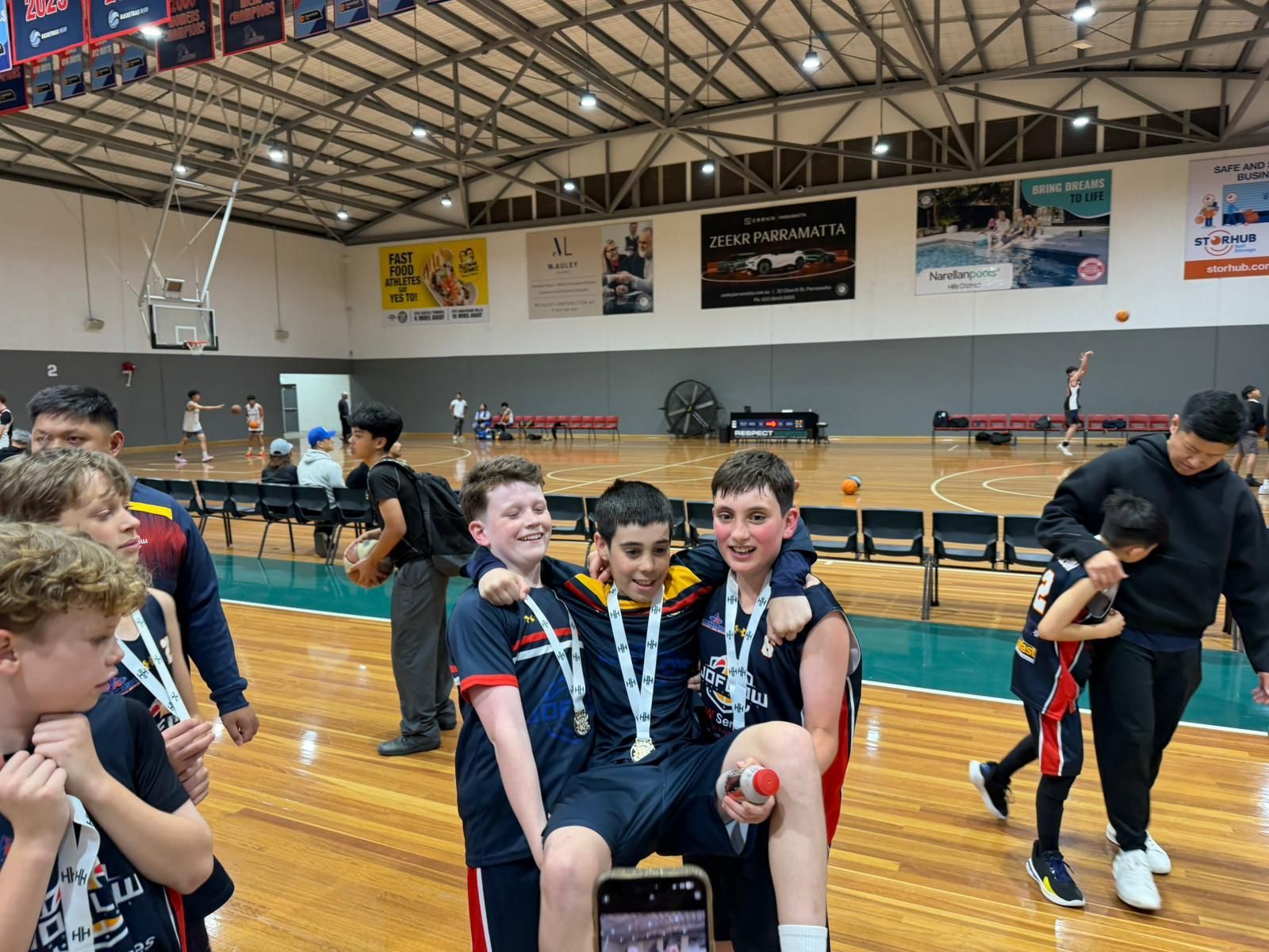 Youth basketball players with medals celebrate victory in a gymnasium.